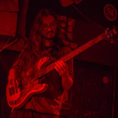 Imagem de Pedro Mariz tocando contrabaixo sob luz vermelha em um palco de pub.