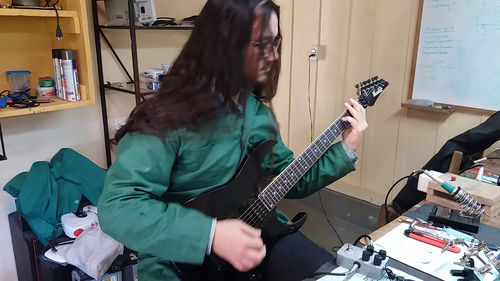 Imagem de Pedro Mariz tocando guitarra e testando pedais em oficina propria.